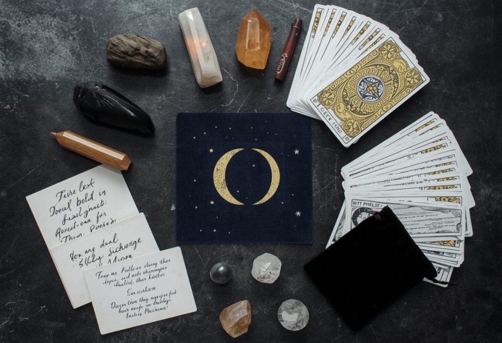 Flat lay of solstice ritual tools with crystals, tarot, moon cloth, notes, and black velvet pouch