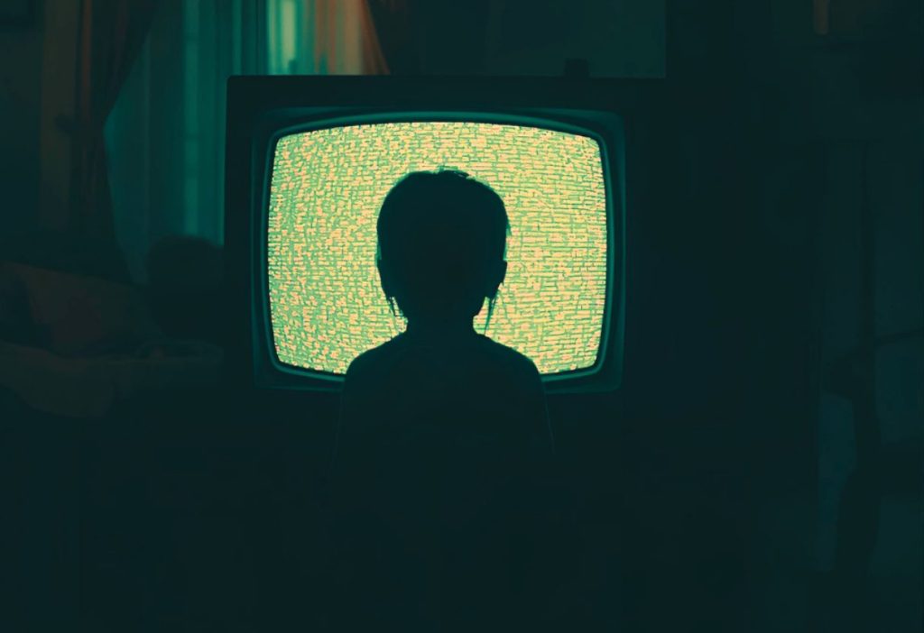 Silhouette of a child staring at glowing static TV screen in a dark, eerie living room.
